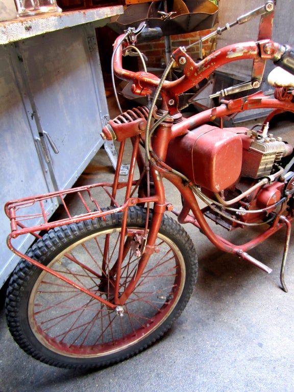 Wow!  Lots of opinions about this bike.  Guessing it is 1940's or 50's, could be earlier.  Briggs and Stratton motor, perfectly worn leather seat.  Carrying bars on front and back.  Lever engages drive system.  More pictures upon request, call for