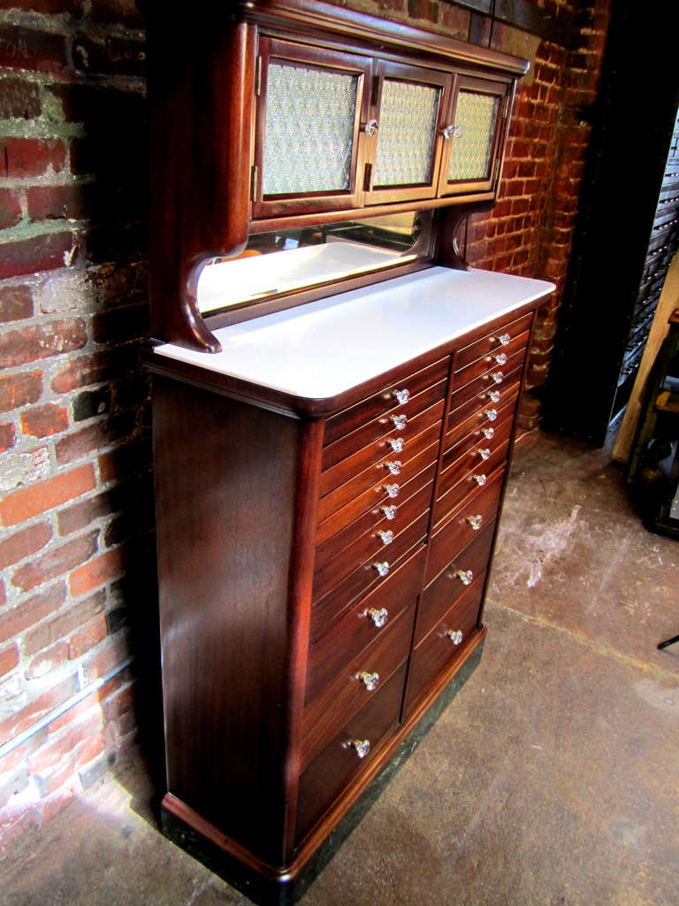 1920's, step back, flame mahogany dental cabinet with 22 drawers.  The original glass knobs dress each drawer with its own piece of jewelry.  The top six drawers have several milk glass tray inserts designed to hold different instruments.  Step back
