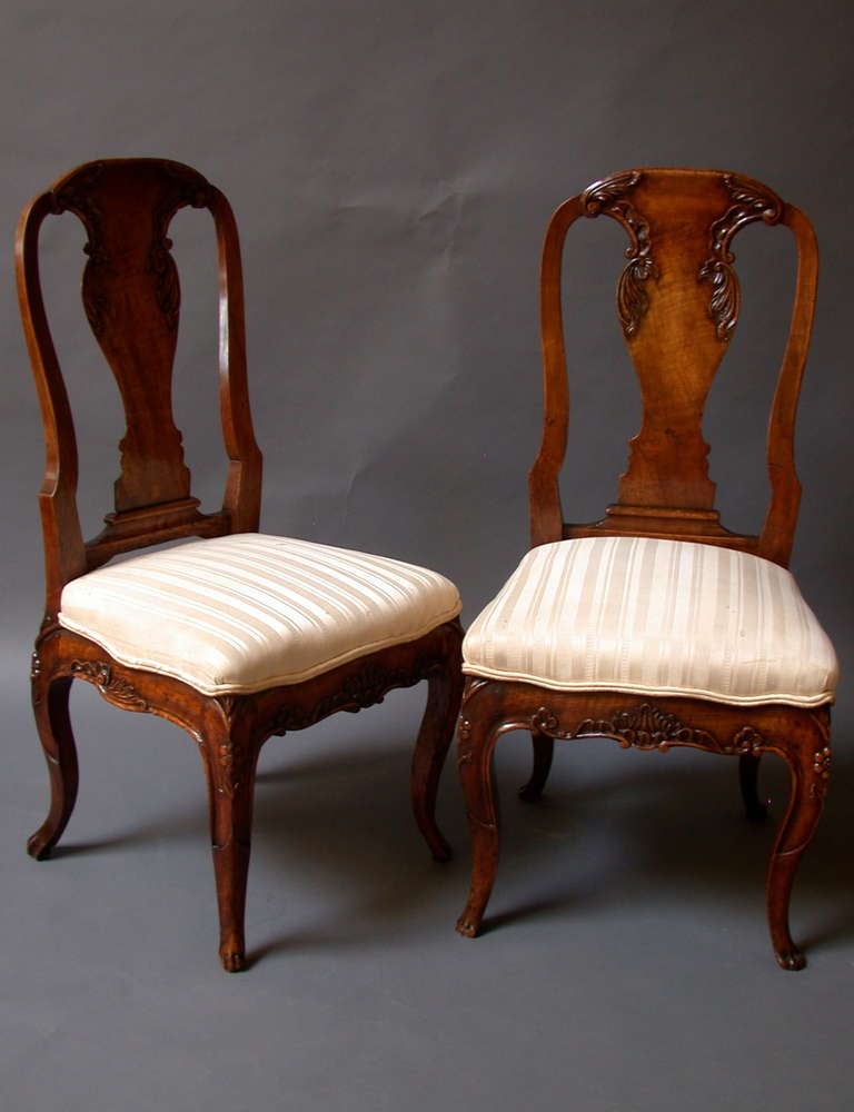Made of walnut with a rich colour and deep patination. The waisted shaping of the backs, echoed in the vase-shaped splats, is a very English form of chair, while the shape of the cabriole legs and the intricate carved decoration are typical of the