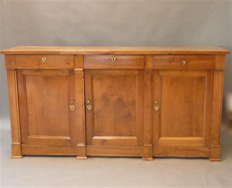 Early 19th Century French “Directoire”Style  Enfilade (Buffet with 3 Doors).  Made of  golden Pearwood with a deep lustrous patination.   Paneled top over three drawers and three cupboard doors divided by flat pilaster columns.  Made in France circa