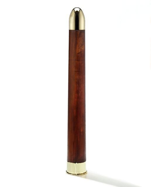 This enormous and sculptural wood and brass artillery shell practice round, made from richly patinated wood with polished brass caps, was designed to simulate the shape and weight of a British anti-tank round. It weighs 57 1/2 pounds.