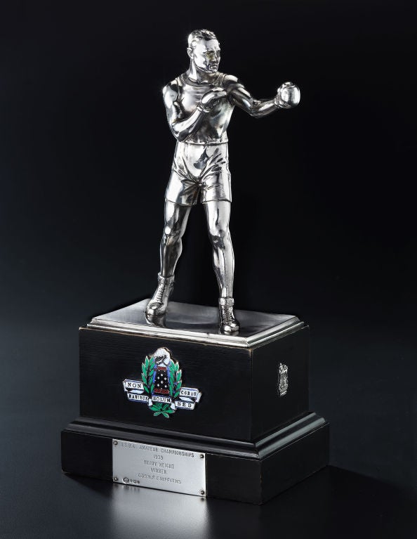 The 1939 British Inter-Services Boxing Association Amateur Championship Heavy Weight Trophy. The realistically modeled silver plated figure of a boxer bearing the hallmarks of the Wurtemberg Electro Plate Company above an enamel plaque with clenched