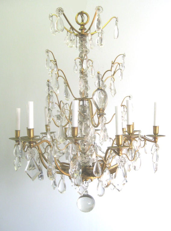 A rare interpretation of a simplified Louis XV chandelier with 12 arms, 2 levels. Also includes 6 lamps in decorative brass enclosure that reflect indirect light on the chandelier. This chandelier has a unique center shaft composed of interlocking