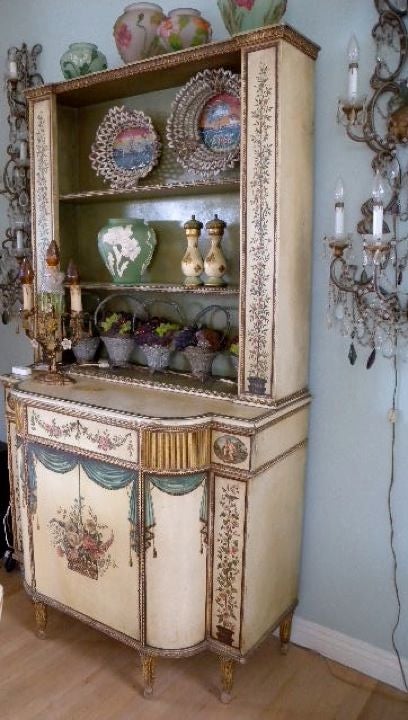A stunning antique china hutch~buffet, hand painted with so much detail, truly makes this “one of a kind”…. The cupboard is a step back, with a demilune base; a single full width drawer separating the top from bottom; and a single door on the base