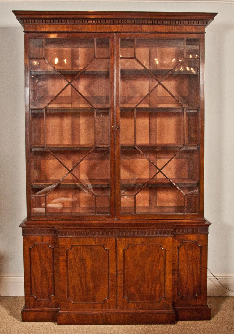 An English George III Period Mahogany Bookcase; the dentil crown above two glazed doors raised on a breakfront base with fluted frieze above four cupboard doors all on a plinth base with an unusual fitted full length drawer. 
Superb period piece