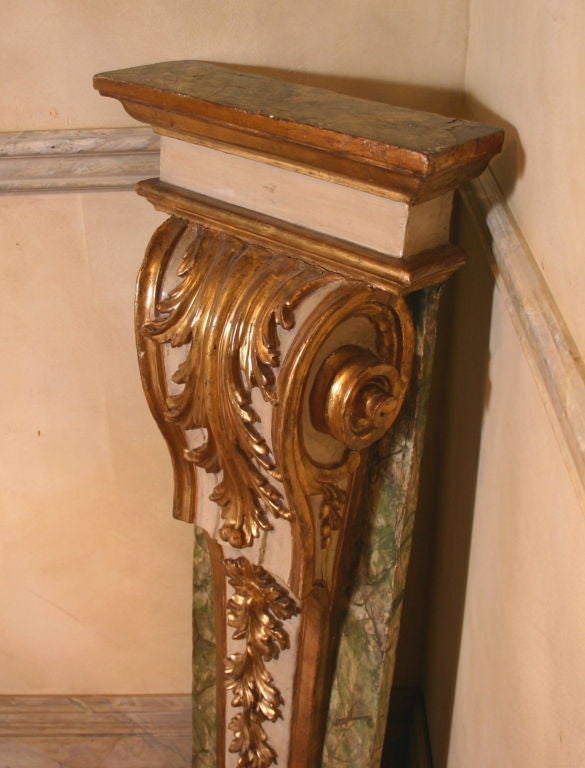 A pair of early 18th century Italian architectural painted and parcel-gilt pilasters having a large carved scroll with acanthus leaves and trailing flowers all surrounded by faux marble decoration.