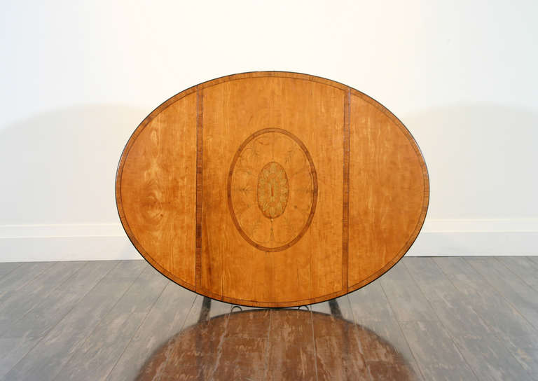 An English late 18th century Sheraton period satinwood oval pembroke table; the tulipwood, ebony and boxwood crossbanded top with oval marquetry inlay in sycamore above a bow fronted, crossbanded drawer flanked by inlaid fluting, raised on ebony