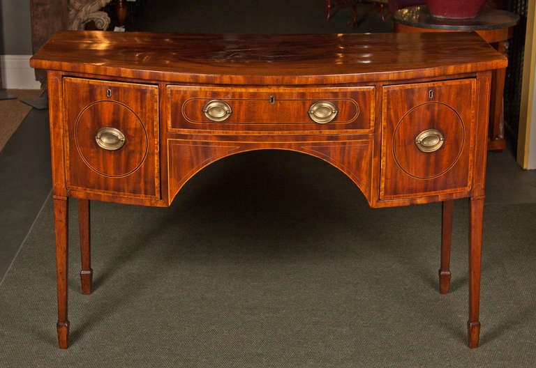 An English late 18th century Georgian mahogany bow front sideboard with boxwood and ebony line inlay and tulipwood crossbanding, raised on square tapering legs ending in spade feet.