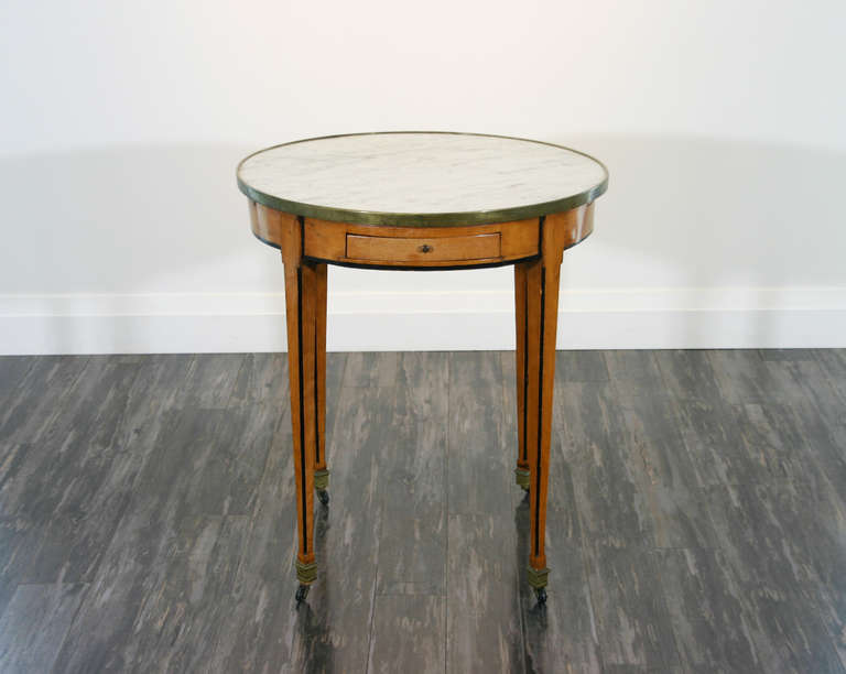 A French early 19th century fruitwood, marble topped faux ebony lined bouillotte table with two drawers and two leather lined and tooled pullout slides above square tapering inlaid legs ending in brass castors.