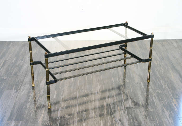 A 1960's Coffee/Cocktail Table by Jacques Adnet, having a glass top to leather wrapped and stitched rails, on brass legs