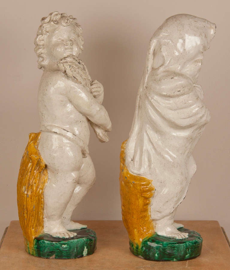 A pair of continental 19th century glazed Majolica putti representing two of the four seasons.