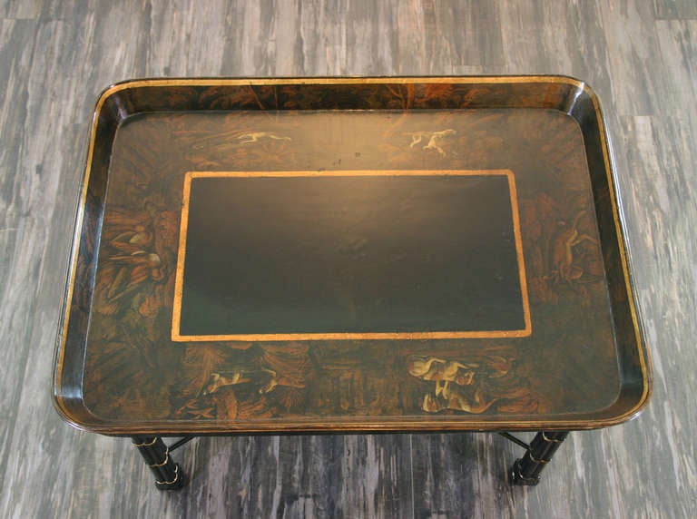 An English Regency period black papier mache Tray on a later bamboo style cluster leg stand; the tray having gilt line decoration and paintings of hounds in landscapes