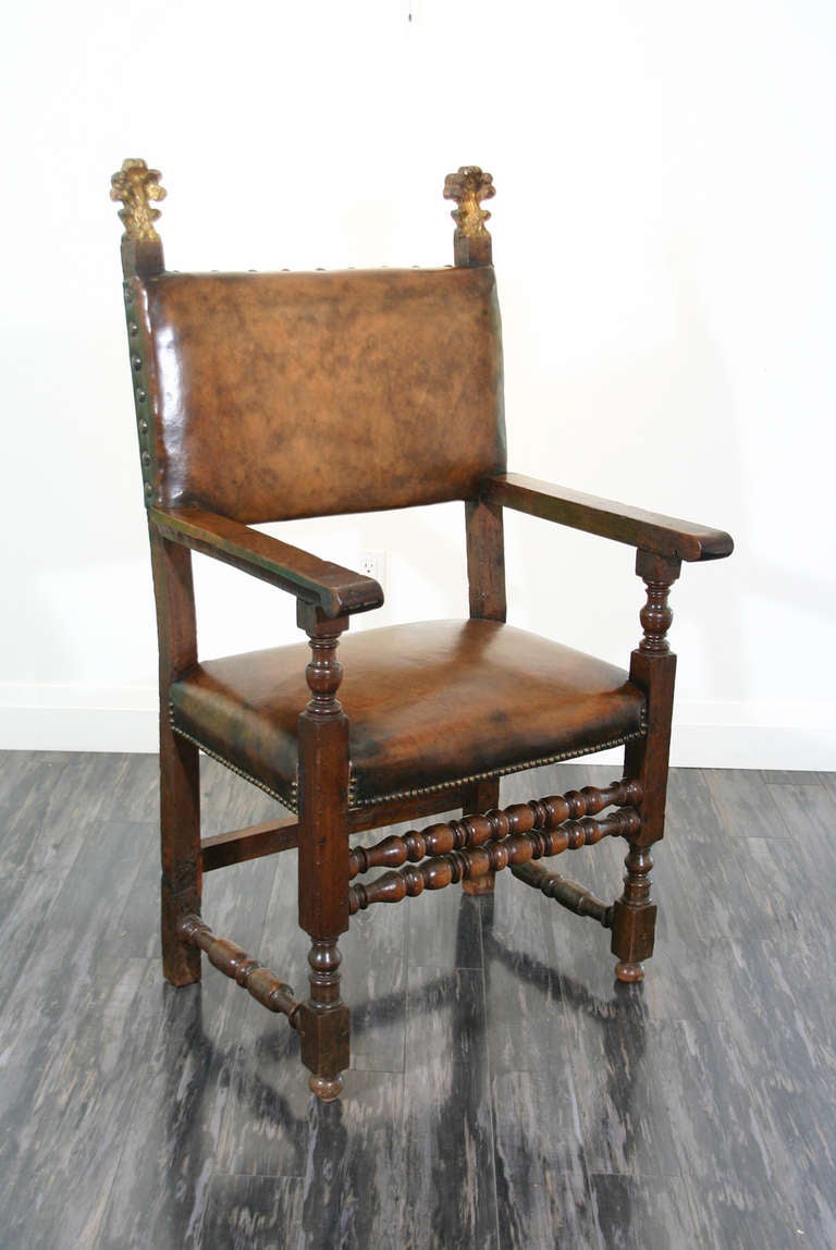 An Italian 17th century walnut armchair with acanthus leaf gilt carved finials and brass nailed leather upholstered seat and back.
