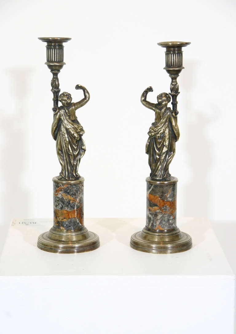 A pair of French early 19th century bronze candlesticks of figures in classical dress mounted on marble pedestals.