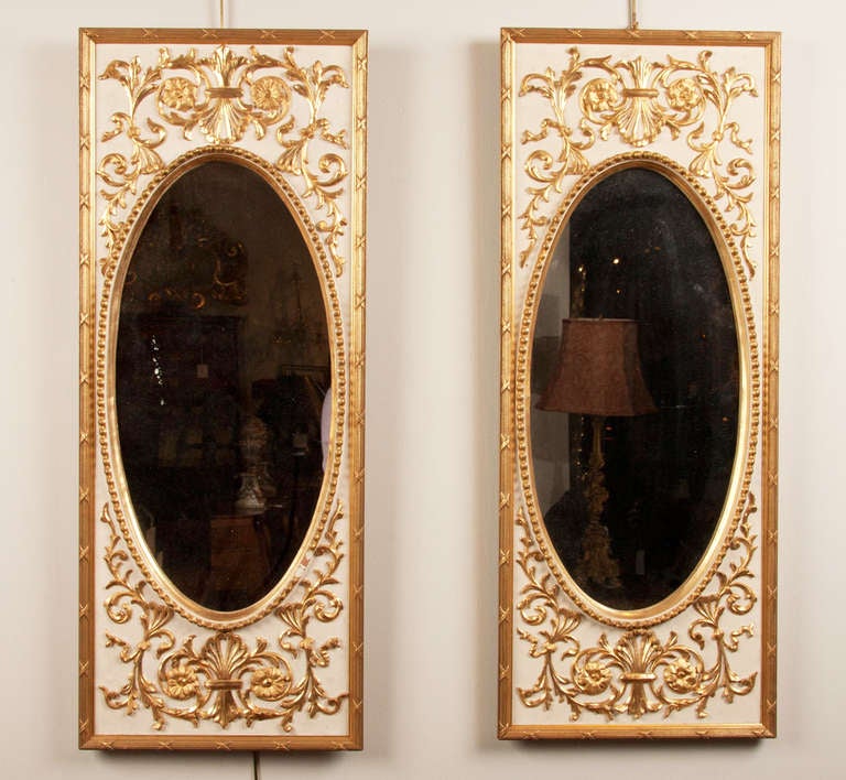 A pair of Napoleon III paint and gilt mid-19th century neoclassical oval mirrors in rectangular frames with foliate and beaded decoration.