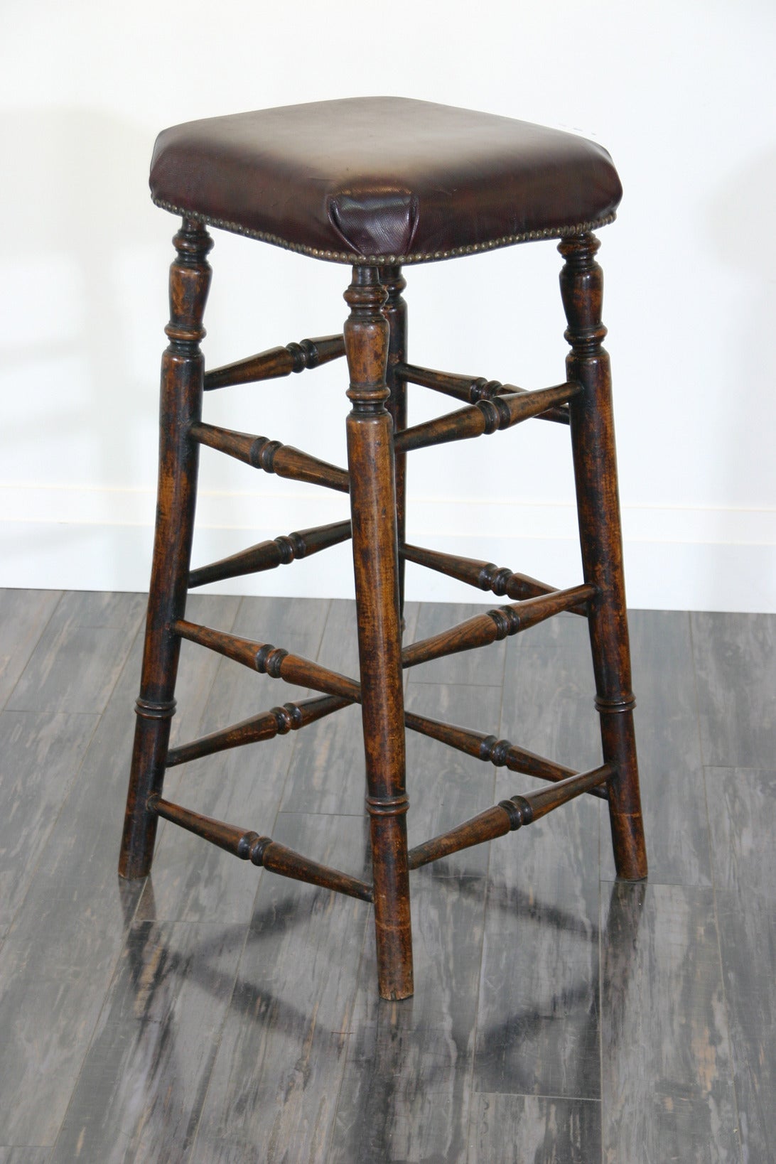 An English late 19th century oak counter stool with leather nailed upholstery.