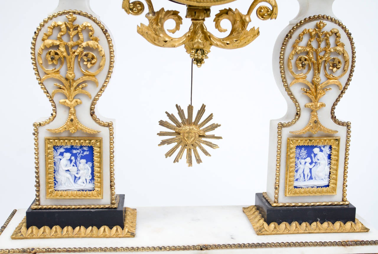 Rare Louis XVI period white marble mantel clock extensively decorated with very fine gilt bronze mounts, the white enamel dial flanked by two neoclassical urns, extensively decorated with fine gilt bronze mounts and Wedgwood cameos depicting