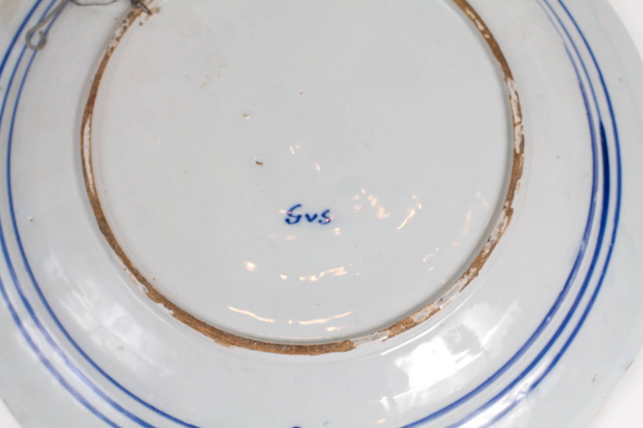 Plat en éventail de Delft avec des motifs floraux présentés comme un paon.
La signature G.V.S est pour Geertruy Verstelle, une femme fabricant de faïence établie à Delft au milieu du 18e siècle sous le signe de 