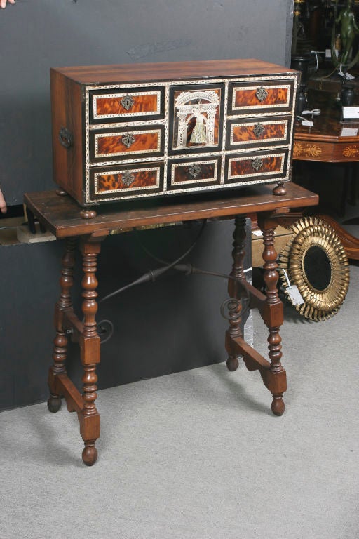 Indo-Portuguese rosewood vargeno, the drawers inlaid with tortoise shell veneer and engraved ivory decorations, fitted with iron corners and handles, resting on a period walnut iron stretcher table.