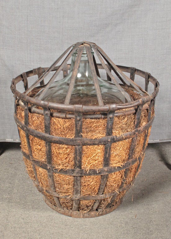 Large vintage wine bottle fitted in its original straw and iron crate.