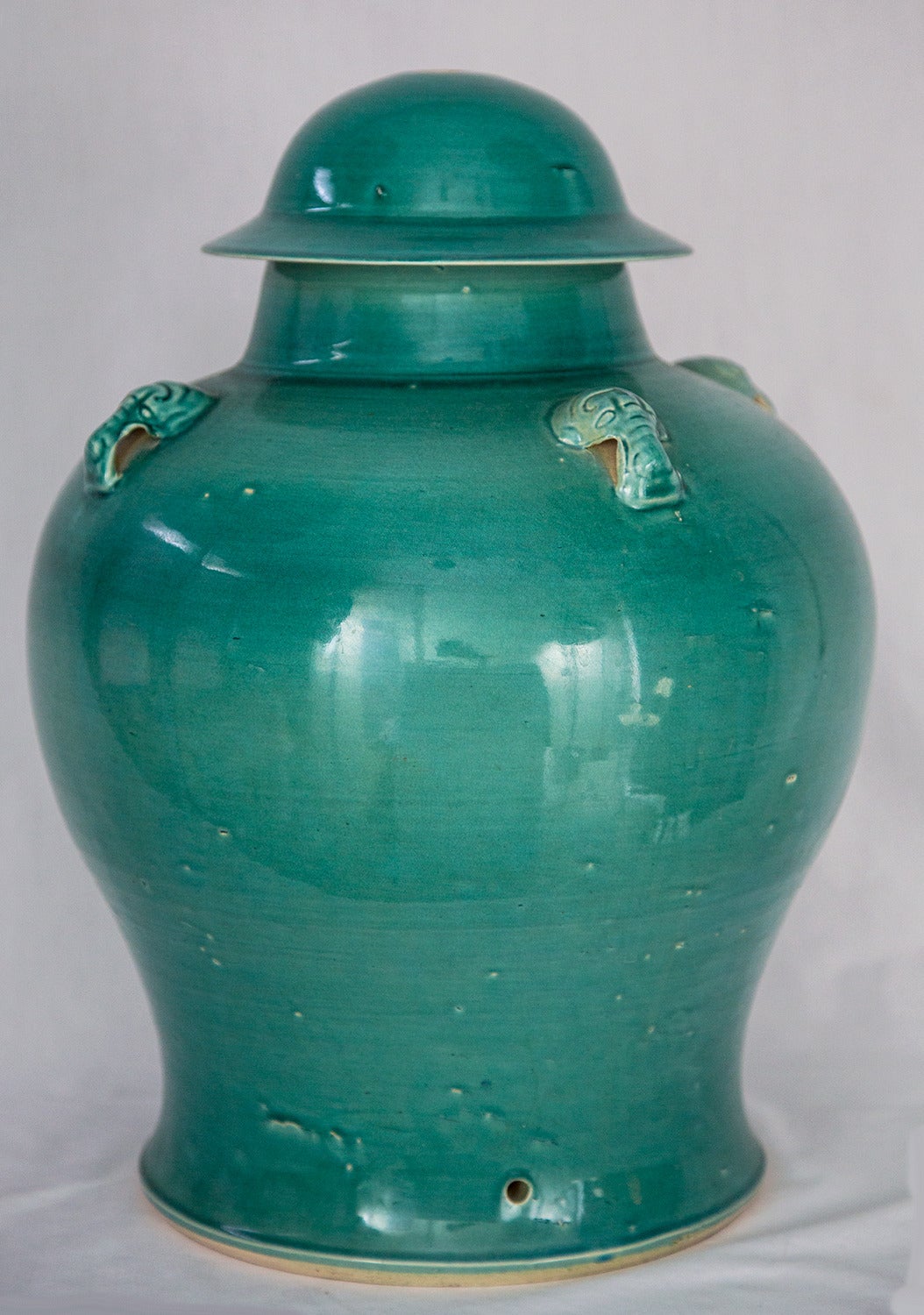 Glazed turquoise-green bulbous stoneware covered floor urn with four raised foo-dog decorations; Factory drilled holes for easy conversion to a lamp, circa 1960s. A wonderful accent for an unused corner of your home that will accentuate the look of