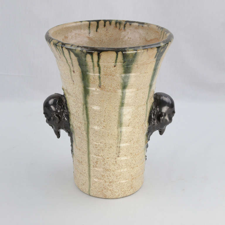 Large two handled art pottery vase, the mottled beige base with visible potting rings and double handles featuring Chinese wise men heads; dripping green glaze over rim. Signed to underside by renowned Belgian ceramic artist and sculptor, Ernest