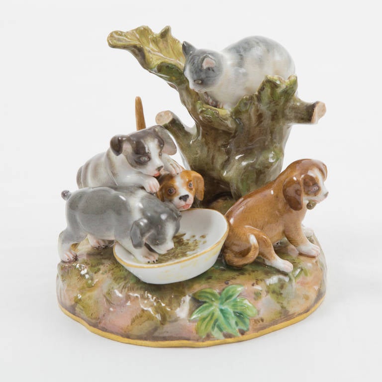 Adorable Meissen Porcelain figurine, beautifully hand painted outdoor scene, depicting four playful dogs on lush grounds, eating and a cat perched on a tree stump, surveying; under glaze Cobalt Blue Crossed Swords Mark also impressed 143 and 130.