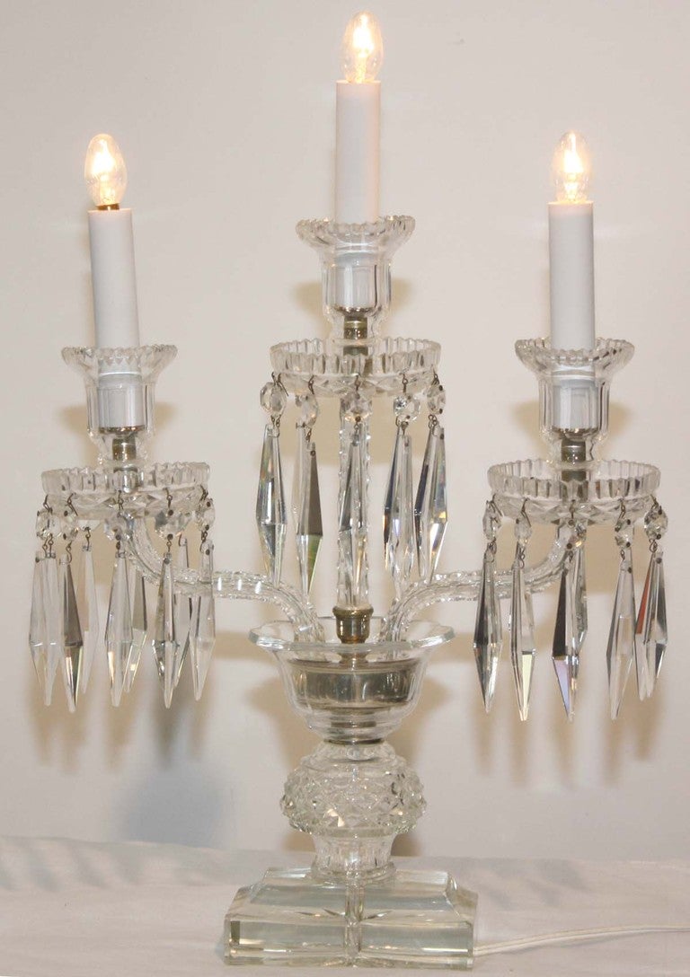 Pair of Continental cut crystal three-light girandoles with crystal pendants on the candle cups; raised on molded glass over diamond cut ball on rectangular base. Created as electrified garnitures.