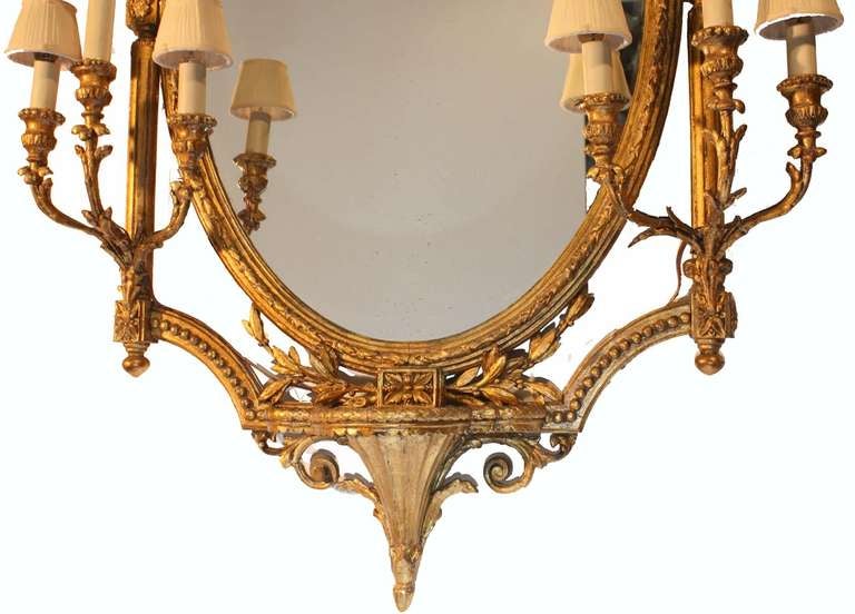 This oval mirror is contained in a highly decorative frame ,flanked by columns, surmounted by an urn shaped crest, and with two three light sconces flanking a lower bracket. A versatile arrangement, that would complement many interiors.