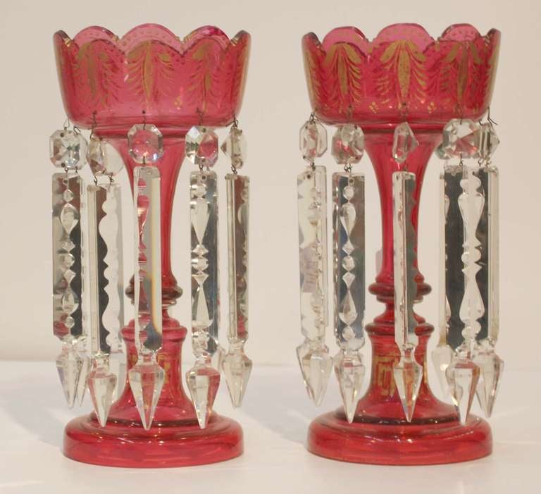 Pair of Victorian ruby glass table lustres with foliate gilding detail around scallop top bowl over shaft, each fitted with ten back notched crystal spears on jewels.
