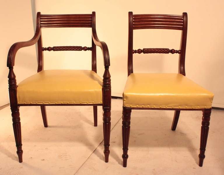 A set of eight English antique mahogany dining chairs, each with rope- carved splat, moulded top-rail and with delicately turned and ribbed front legs, The stuffover seats are upholstered in yellow faux leather. There are six side chairs and two