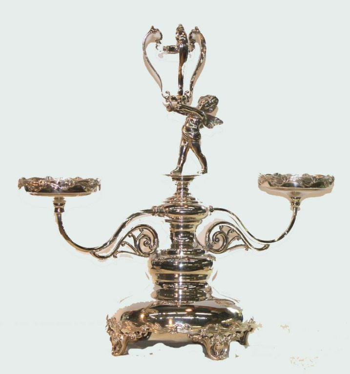 Canadian silverplated epergne, the stem modelled as a cherub upholding a trumpet-shaped vase flanked by two scrolling arms supporting detachable bowls. Stamped.:Toronto Standard Silver Co.

This is for both flowers and fruit and makes a spectacular