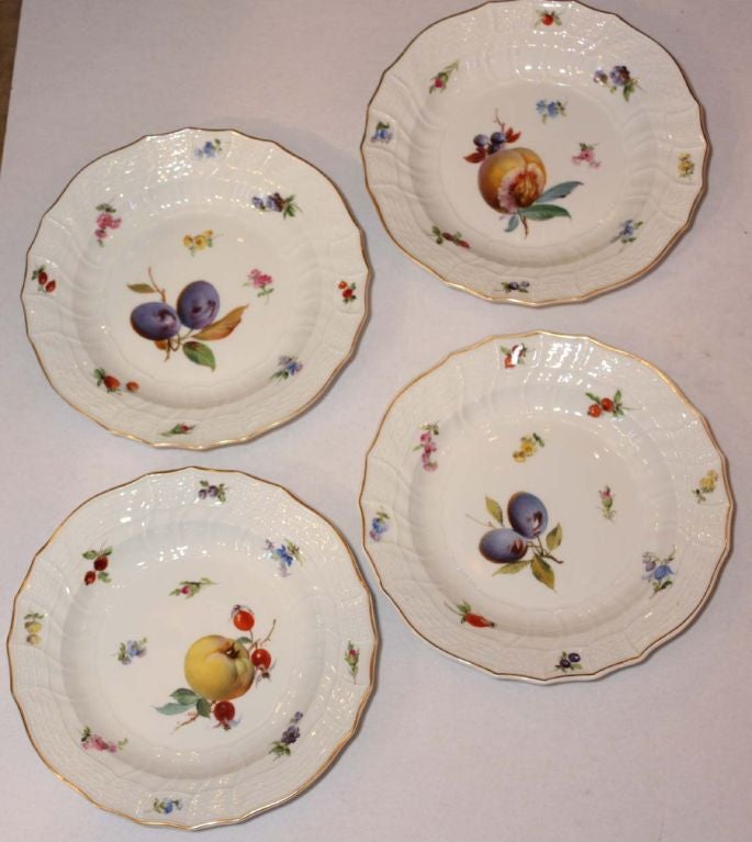Set of ten individully painted plates depicting fruits and scattered with small flowers,within a basketwork border edged in gilding; reverse with underglaze blue crossed swords, impressed numbers.