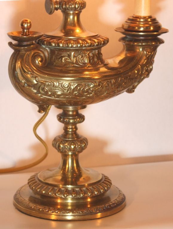 Such a fine quality lamp was sufficiently impressive to be retailed by Tiffany. The adjustable  lamp is boldly cast with  scrolls and masks and raised on a circular and stepped foot. Although in the style of an oil lamp it was always fitted for