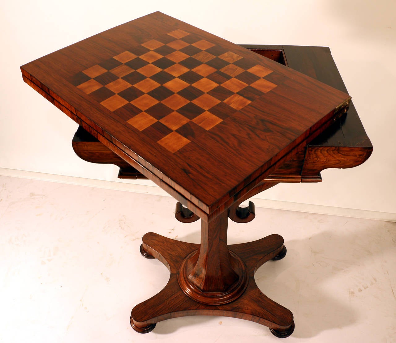 A William IV rosewood fold-over chess and card table, the surface inlaid with a board for chess, and opening to reveal a green baize surface for cards, with storage compartment beneath, the whole elegantly supported by a tapering and paneled column