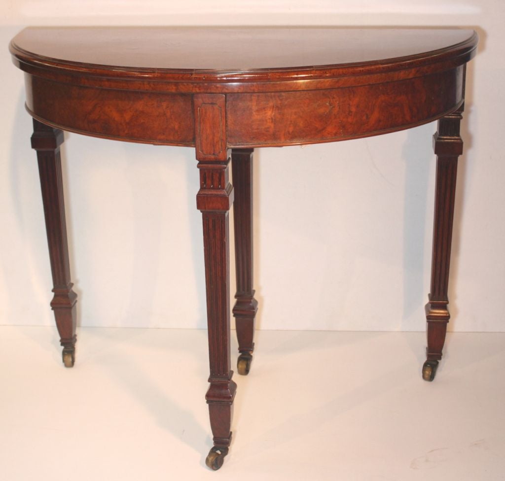 William IV figural walnut demilune table opening with sliding leg to circular baize inlaid and walnut bordered games table, raised on four square fluted legs set into apron and mounted on brass casters.