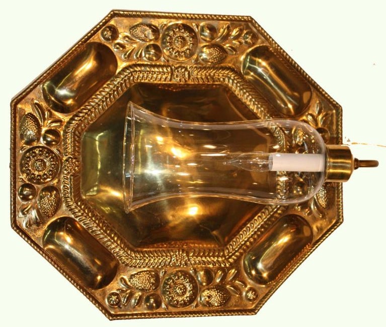 Pair of Scandinavian octagonal brass reflector plates embossed with lozenges divided by flowers and berries, with gadrooned borders; adapted to electricity with later candle arm extending to clear glass hurricane shade.