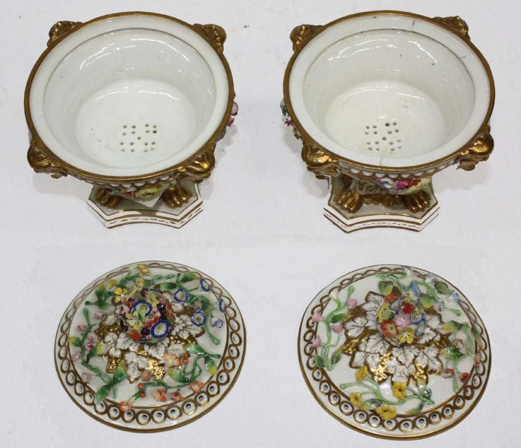 Pair of Derby porcelain potpourris and covers, the bowls with applied flowers, and pierced rims accented with four gilded masks, supported on paw feet over shaped bases; the covers similarly applied and pierced, with floral knops.