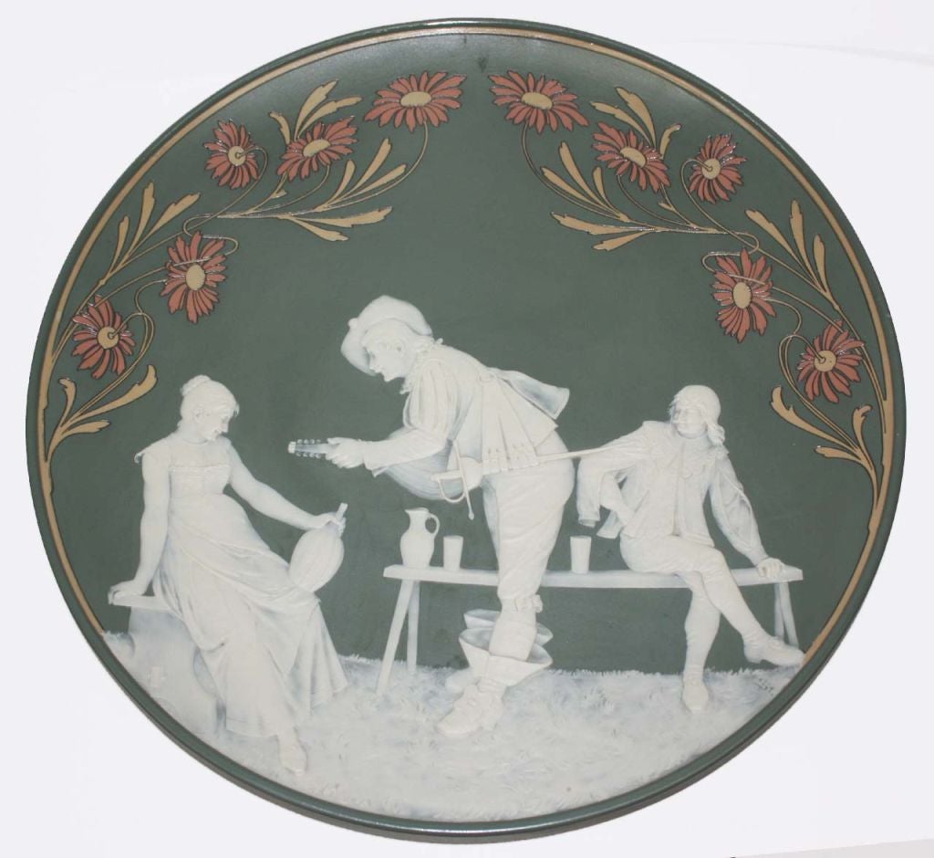 Mettlach green matte glaze stoneware charger with cameo vignette of troubadour serenading a young woman (model 2795) and incised floral border. Pierced on back for hanging. Backstamp with Mettlach abbey over Mettlach and VB (Villeroy & Boch.)