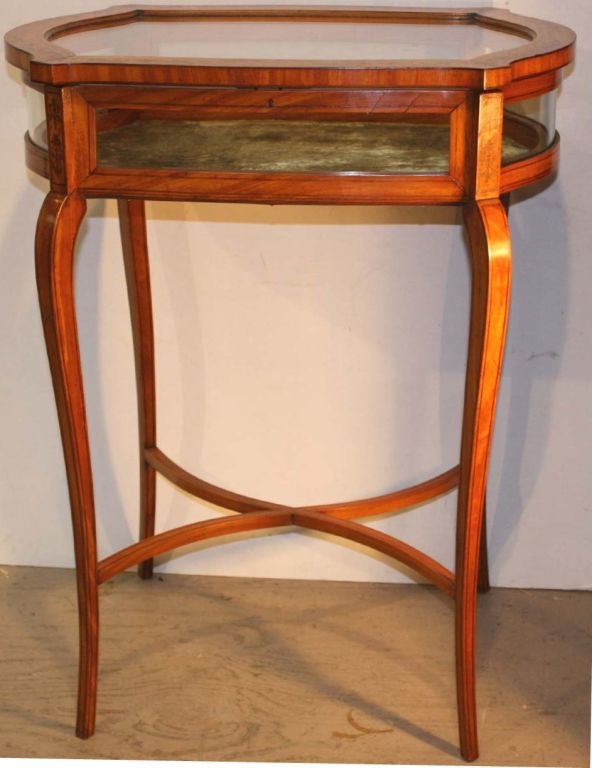Edwardian satinwood display or bijouterie table with marquetry and stringing, the locking lift top fitted with curved front and back panes, the sides being of serpentine glass, the interior base lined with bronze color velvet, raised on cabriole
