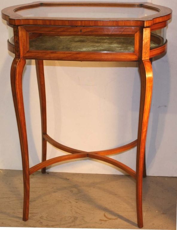 Mesa de exposición o bijouterie eduardiana de madera satinada con marquetería y encordado, el tablero elevable con cerradura provisto de cristales curvados en el frente y el fondo, los laterales de cristal serpentinado, la base interior forrada de