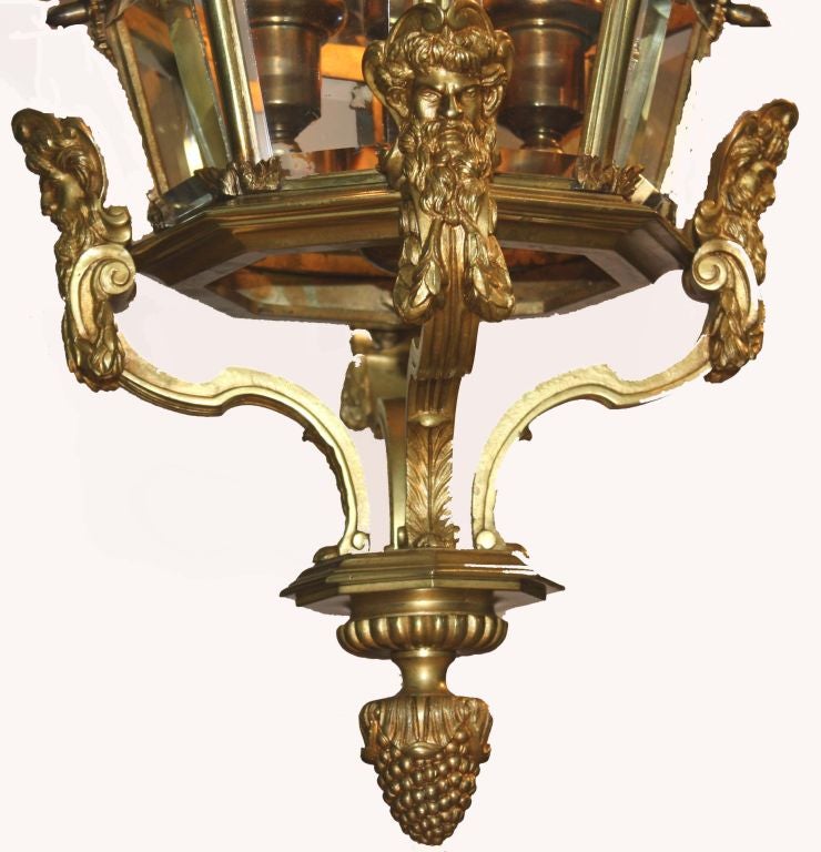 Louis XIV style octagonal gilt bronze three-light Versailles lantern with four levels of graduated bevelled glass panels descending from corona and mounted by shell forms, supported by four mask form straps terminating in grape cluster finial.

The