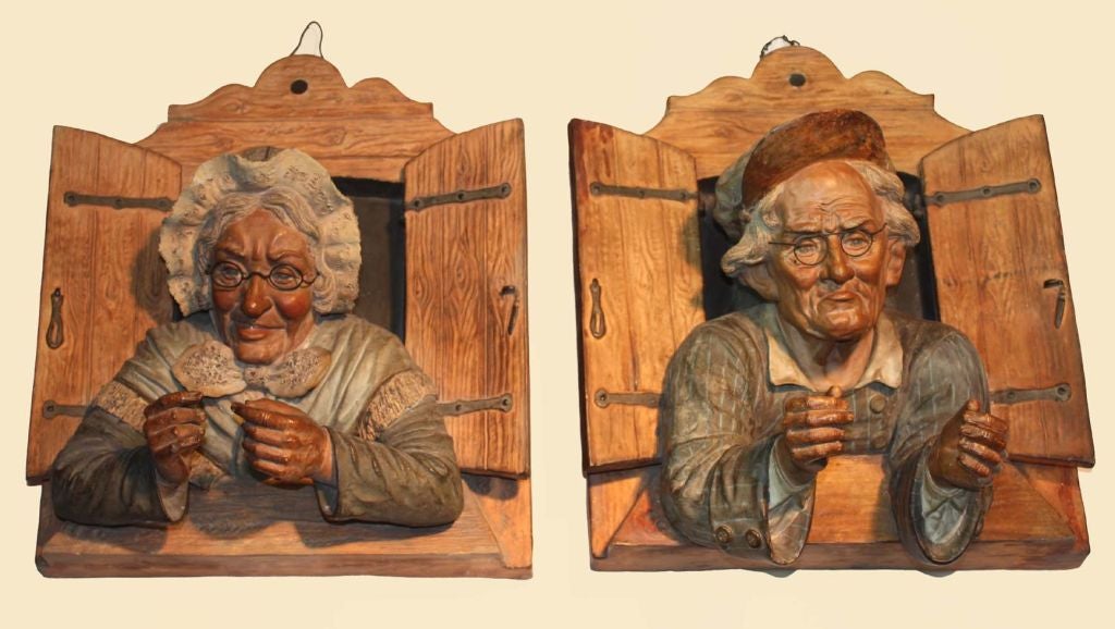 Pair of terra cotta wall plaques modelled in high relief and painted, portraying an old couple looking out the window.