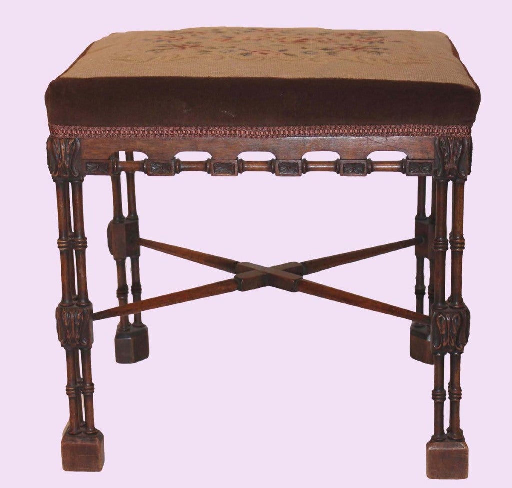 Victorian walnut stool in the Chippendale style with floral needlepoint stuff over seat bordered in brown velvet, raised on cluster column legs, joined by X-stretcher, with block feet.