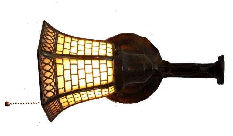 Pair of wrought iron wall sconces with bell form caramel leaded slag glass shades, the shades stamped Handel.