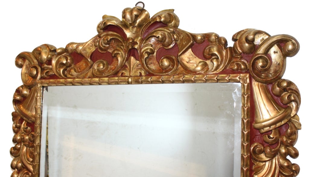 Miroir biseauté de style baroque dans un cadre en bois sculpté peint et doré, avec une crête d'acanthe sur des bordures feuillagées avec des détails de fruits. 