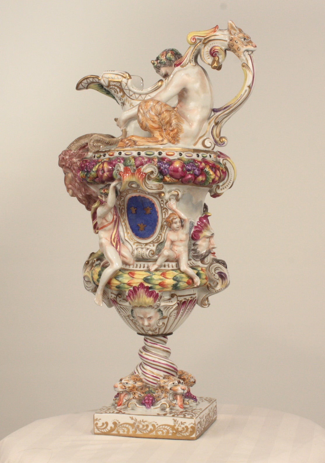 Antique Capo Di Monte porcelain figural ewer, exuberantly modeled with a satyr, putti. various figures and fruit, also with the Royal arms of the Bourbons, raised on a square pedestal modeled with leopard heads, marked underneath with a blue N