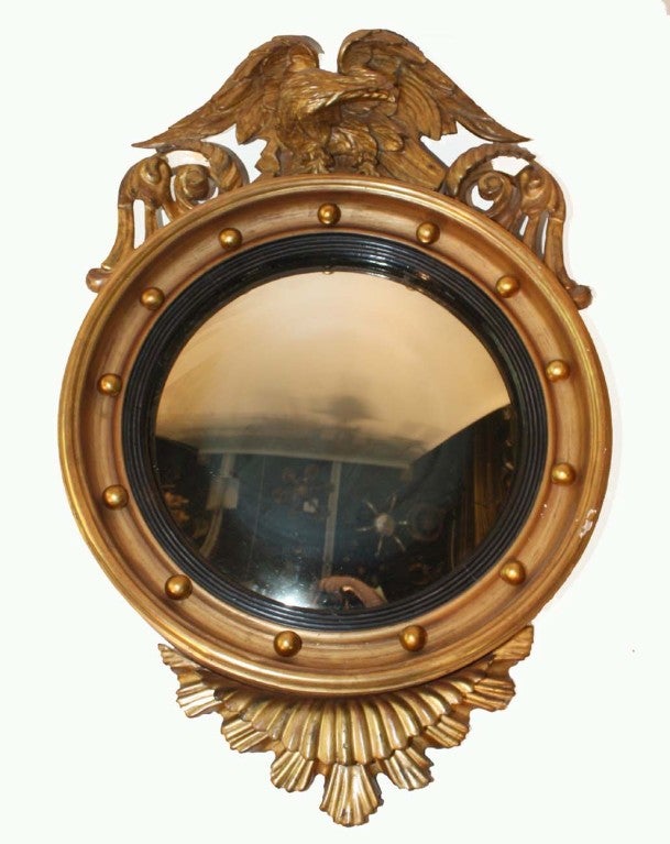 Federal style giltwood and japanned convex mirror with carved eagle crest. These mirrors, also called butler's mirrors, were popular in Europe and North America in the late 18th century and early 19th century. This 19th century mirror has 13 gilded