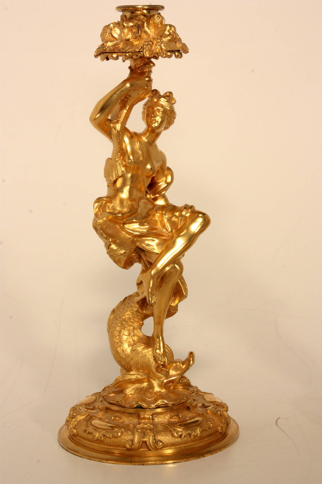 A pair of antique French gilt bronze figural candlesticks playfully and crisply modeled after Clodion, one as a satyr astride a lioness, the other as young woman astride a dolphin, each on matted and repousee circular base and with bobeches modeled