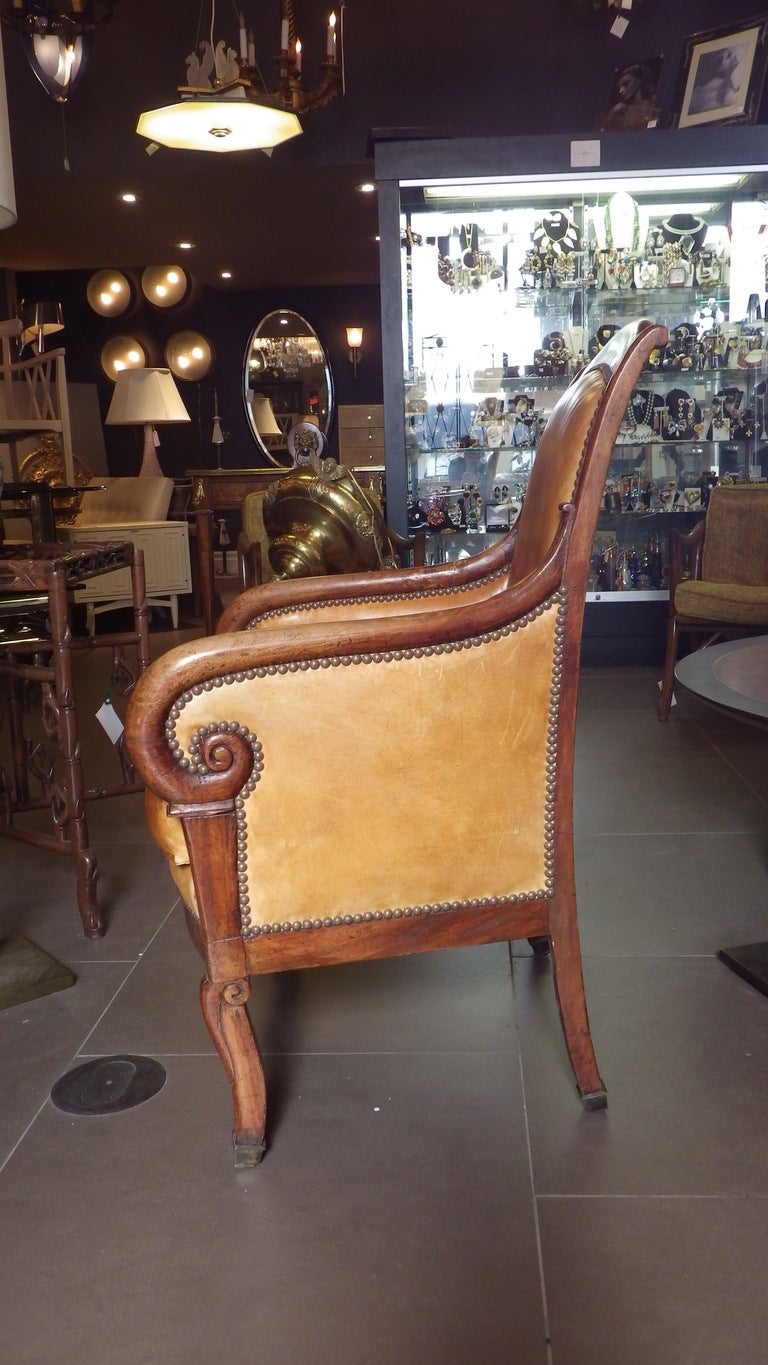 Beautiful leather chair with burnt orange leather,  natural wood finish, and brass bolting.